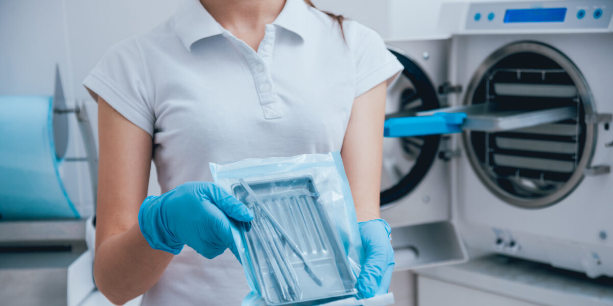 A nurse holding a tray packed in SBS standing in front of a sterilization machine.